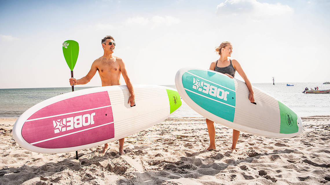 Ein Paar trägt Supboards am Strand